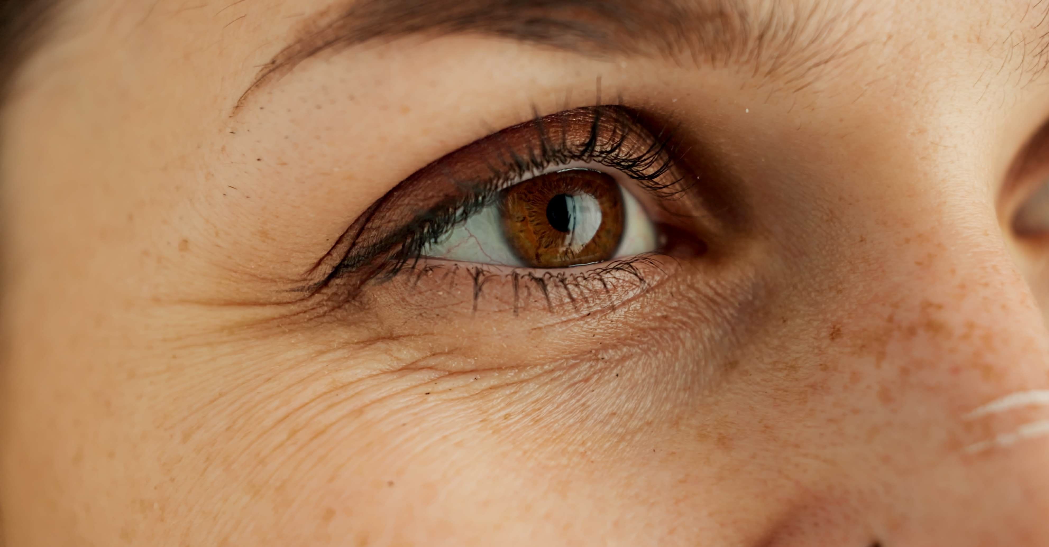 Nahaufnahme eines Auges, das an der Kamera vorbeischaut. Kleine Fätchen um das Auge herum zeichnen sich ab und zeigen erste Anzeichen der Hautalterung.